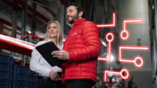 EIn Mann und eine Frau stehen mit Klemmbrett in einem Lager. 