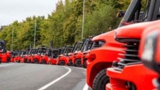 Viele Gabelstapler von Linde Material Handling aufgereiht auf einem Parkplatz.